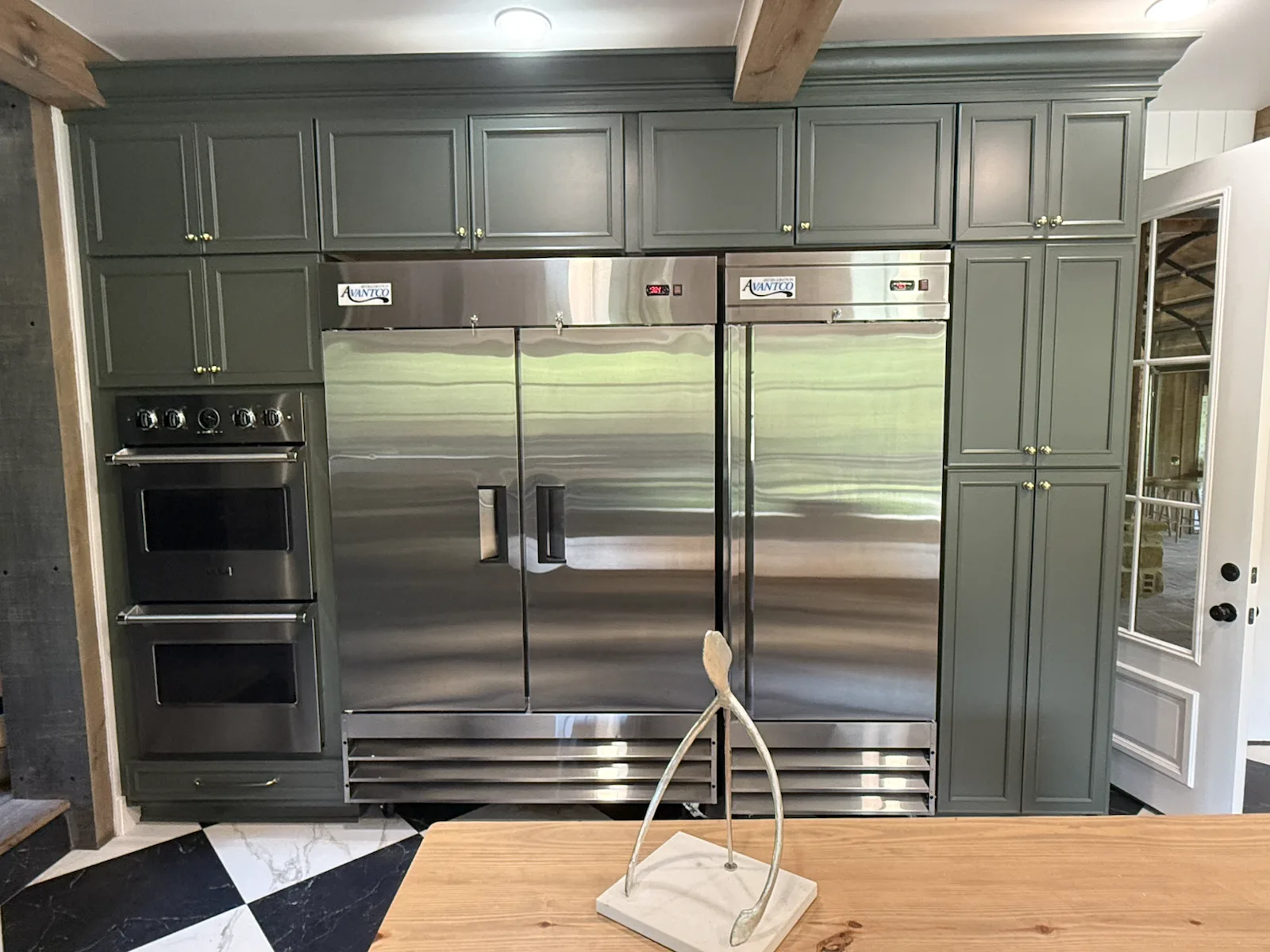 Cortina stainless refrigeration wall with double ovens and green cabinetry