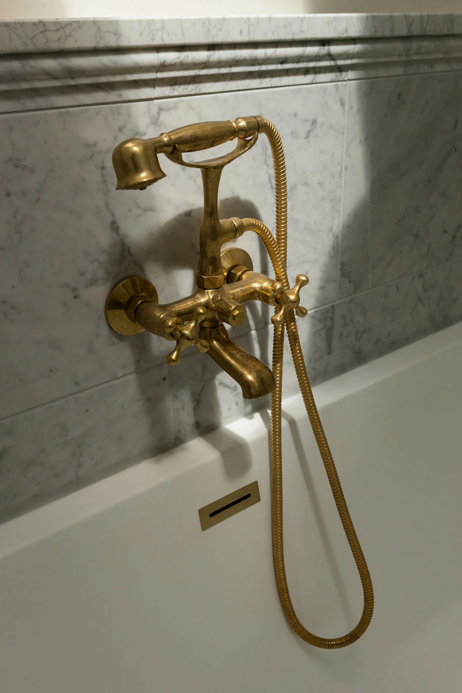 Riverview bathtub with brass fixtures and marble tile surround